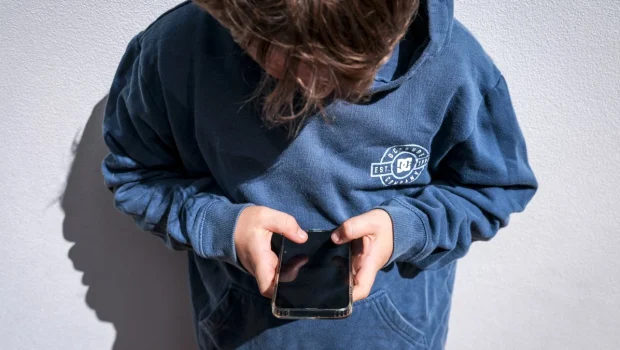 هاتف ذكي على مكتب خشبي بجانبه كتب تعليمية تعبيراً عن الحماية الرقمية للأطفال