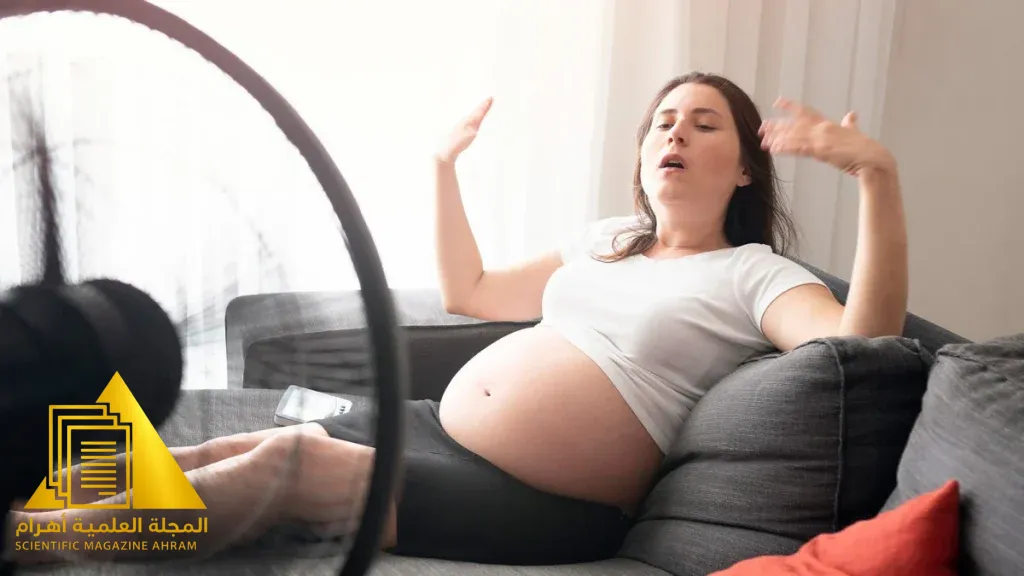 امرأة حامل تبدو مرهقة وتجلس في جو حار وتشرب الماء